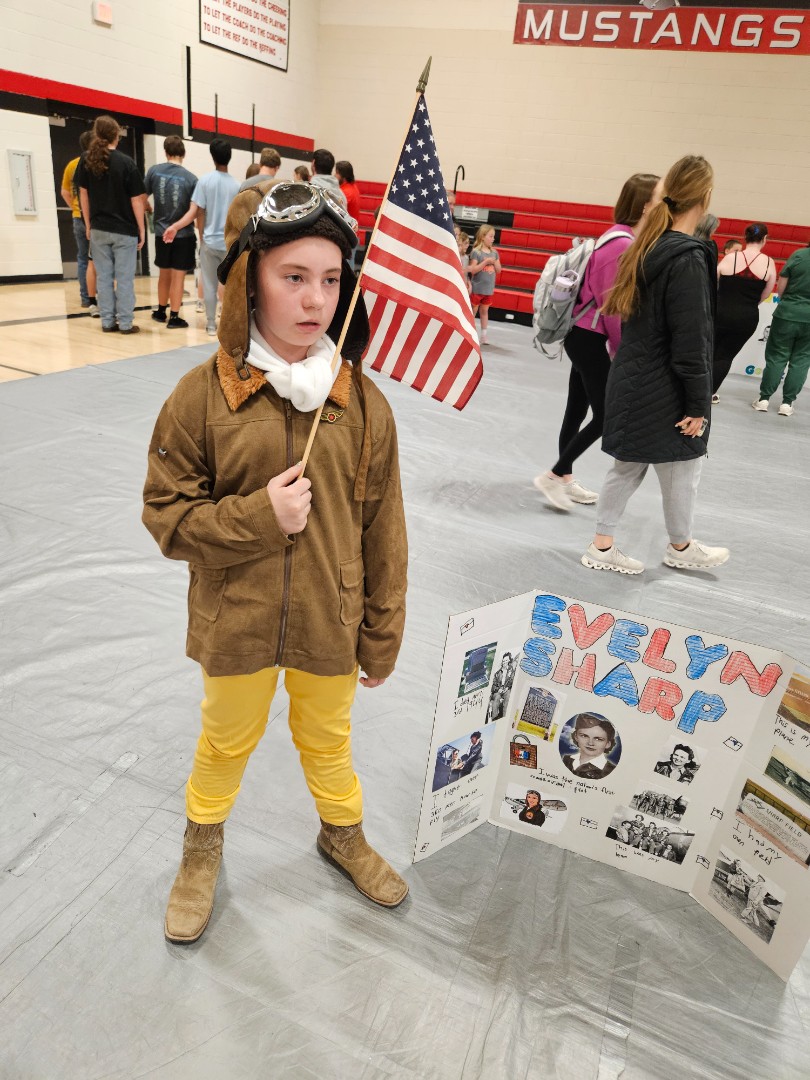 A young boy in a colorful costume proudly holds an American flag, smiling at the camera.