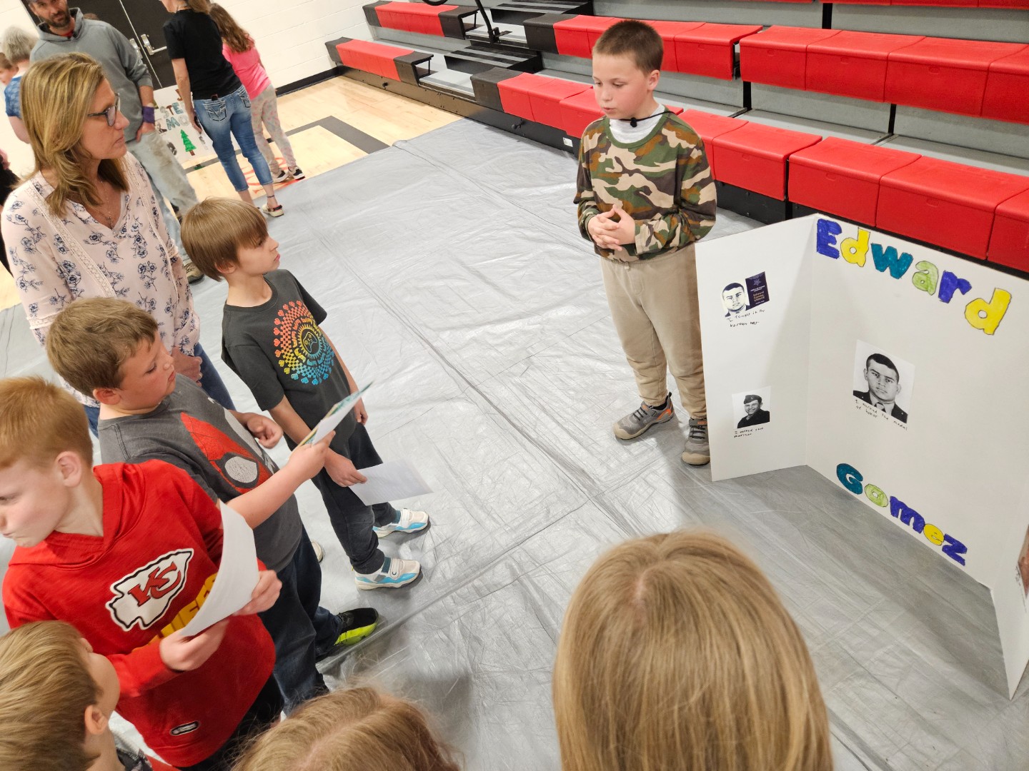 A group of children gathered around a poster board, engaged in discussion and pointing at various sections of the display.
