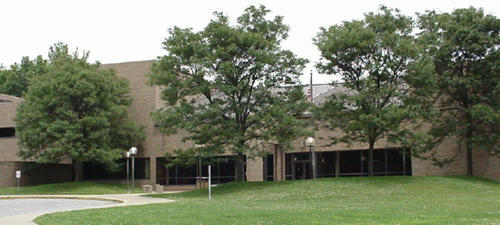 A view of a modern building surrounded by green grass and trees, with large windows and a simple architectural design.
