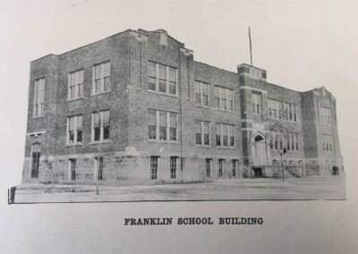 A historical black and white photograph of the Franklin School Building, showcasing its brick architecture and large windows.