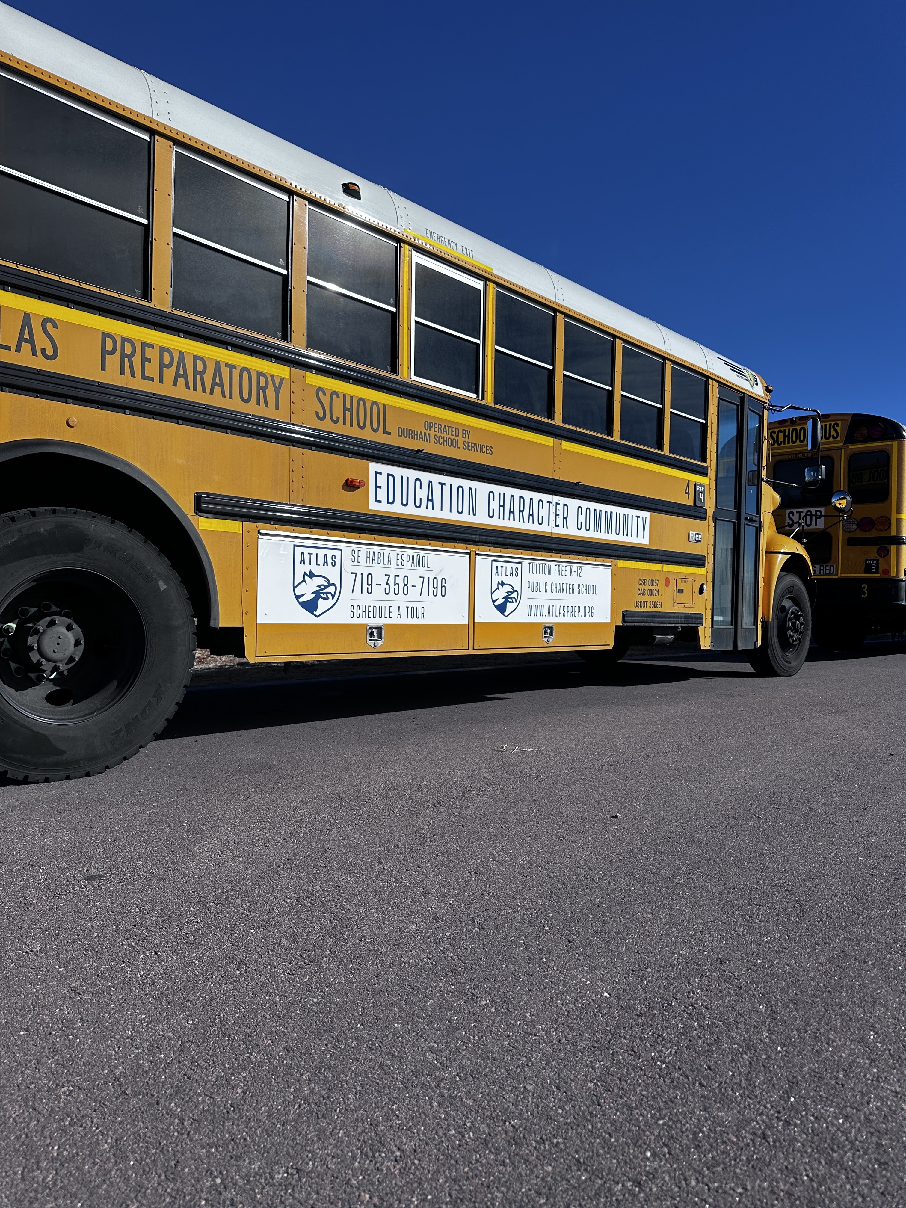 A side view of a yellow school bus parked on a paved surface, with a clear blue sky in the background.