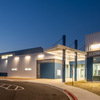 A modern building exterior illuminated at dusk, featuring a curved driveway and a covered entrance with columns.