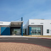 A modern building with a blue and white exterior, featuring large glass windows and a welcoming entrance, set against a clear blue sky.
