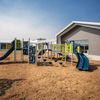 A colorful playground featuring slides, climbing structures, and swings, set against a clear blue sky and a modern building in the background.
