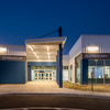 A modern elementary school building illuminated at night, featuring a large entrance with glass doors and blue accents.