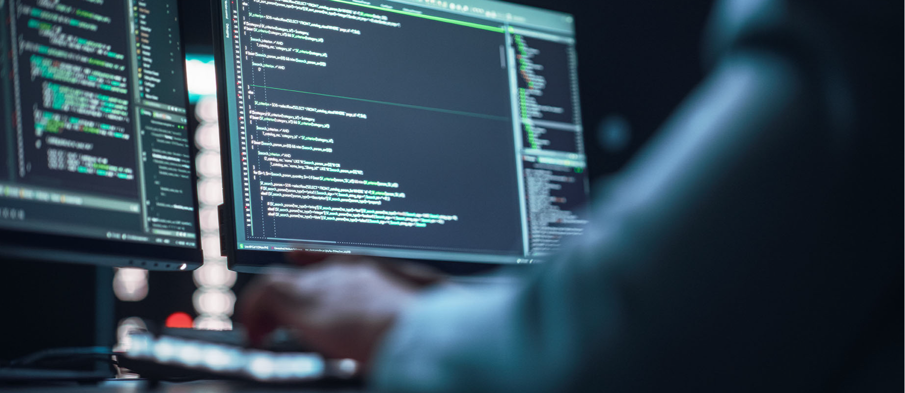 Coding language on two computer monitors with hands of computer technician on keyboard