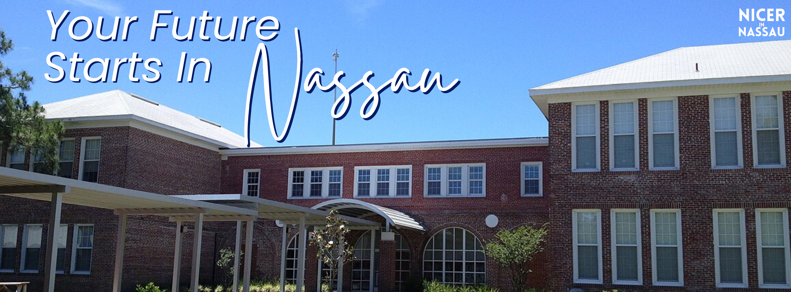 Exterior of a red-brick school building on a sunny day with a wide sidewalk, covered walkway, and manicured green lawn in front.