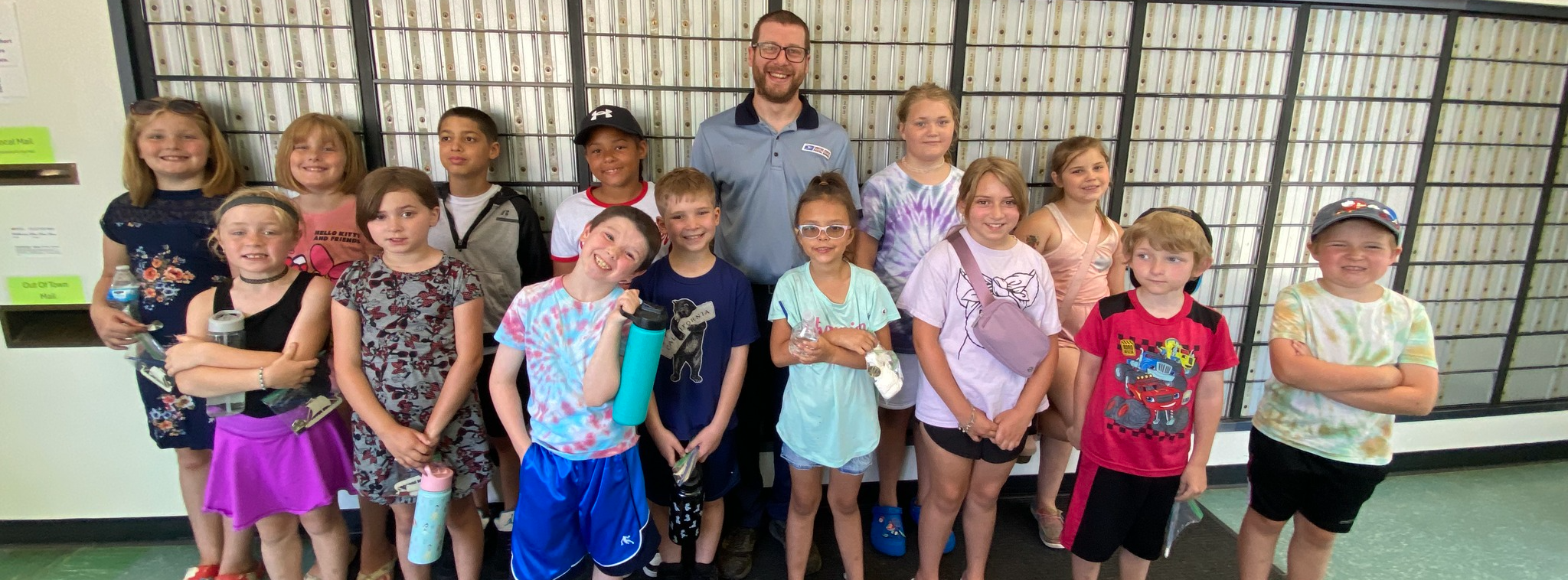 Students pose with a postal worker in front of PO Boxes at the Friendsville Post Office.