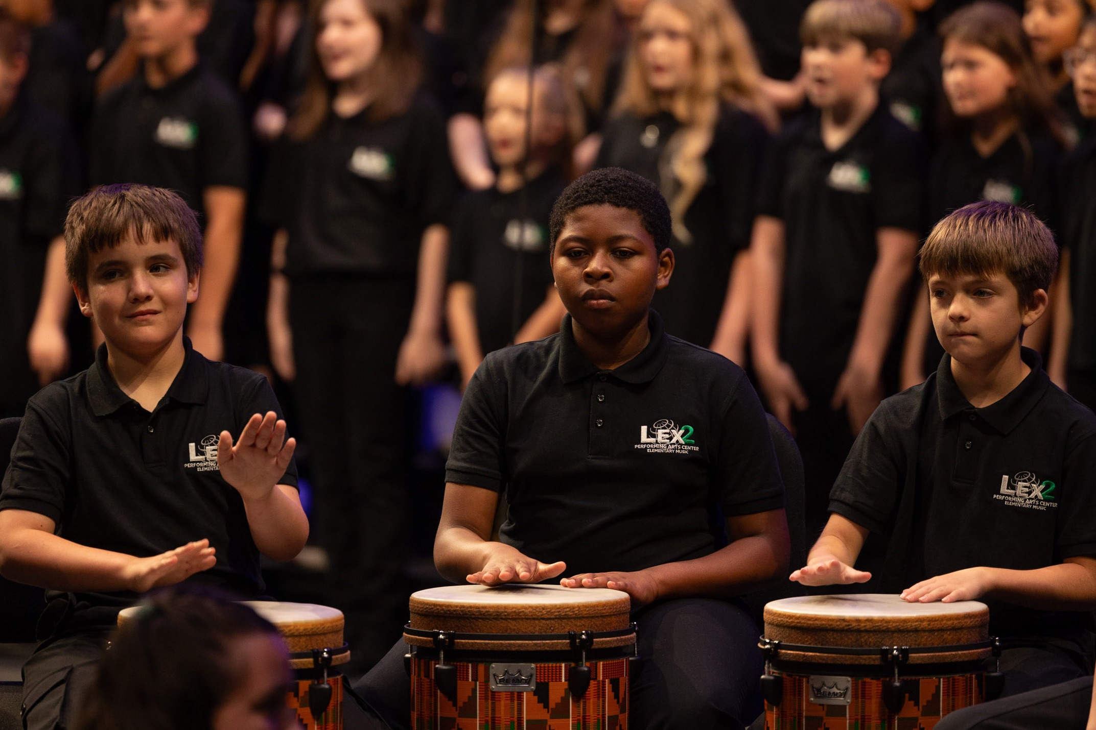 3 drummers play on stage, chorus in background