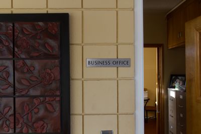 A sign labeled 'BUSINESS OFFICE' is mounted on a wall next to a textured artwork, with a doorway leading to another room in the background.