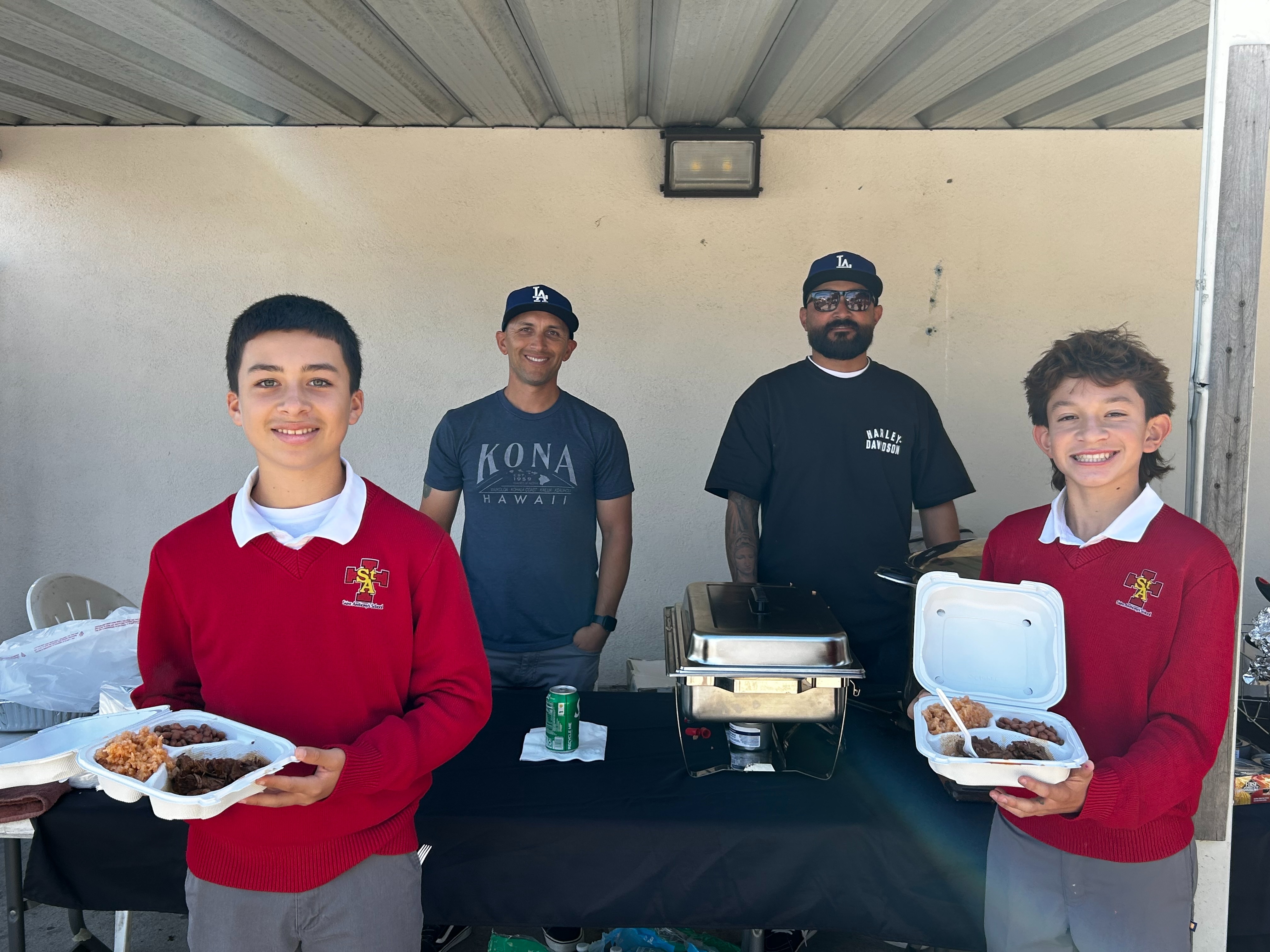 Four students stand in front of a wooden altar with a crucifix, dressed in school uniforms, with their hands clasped in prayer.