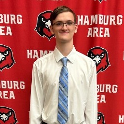 Benjamin Vees smiling with a hamburg hawks media wall in the background.