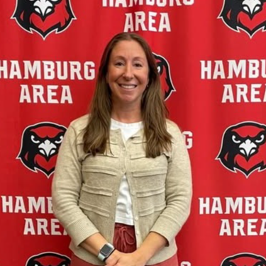 Jodi Petrie with straightened hair smiling on a hamburg area hawks media wall behind her.