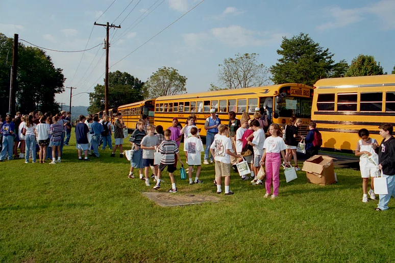 A students walking and talking on grass next to a school buses.