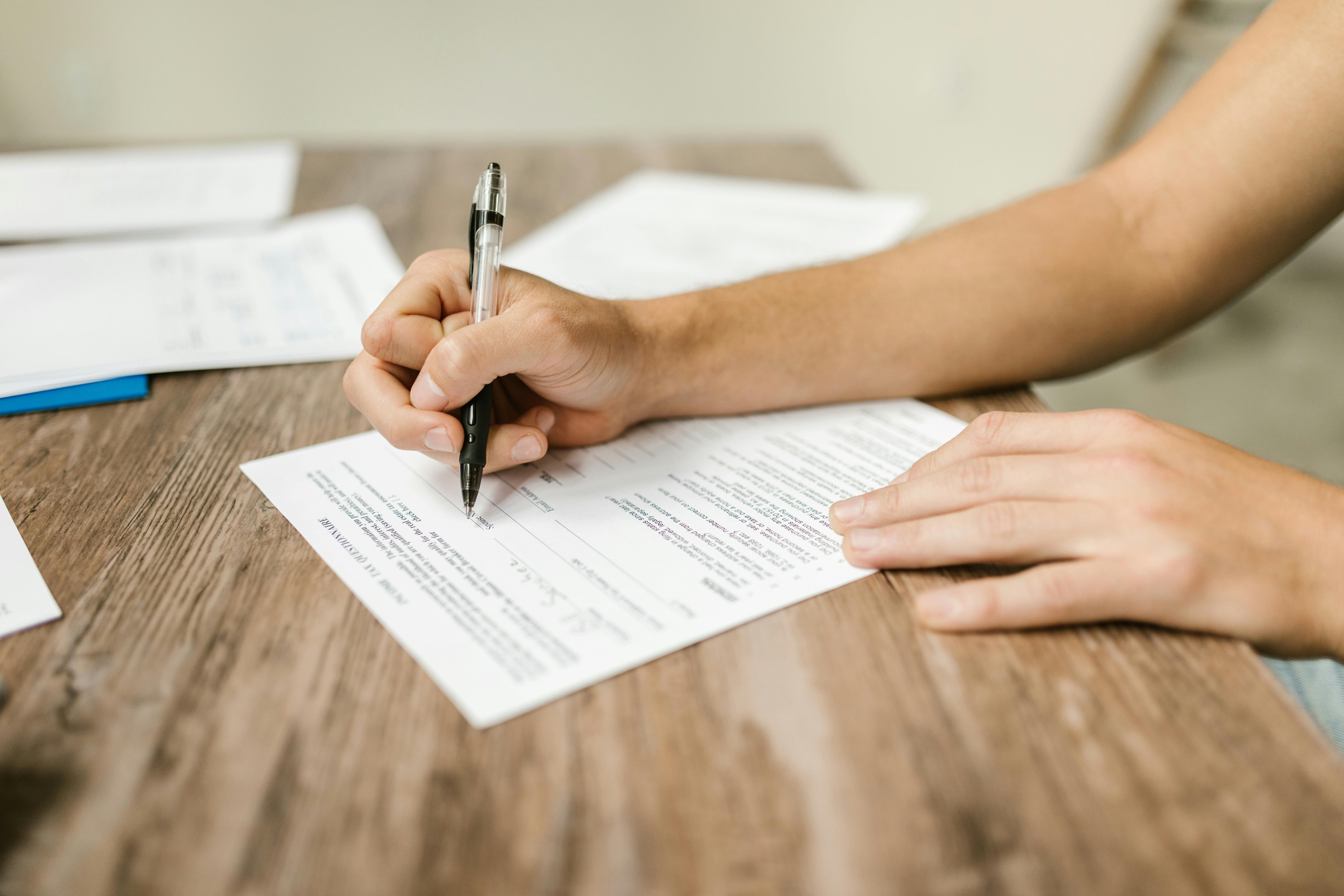 A person filling out a form with a pen, with other forms around it.