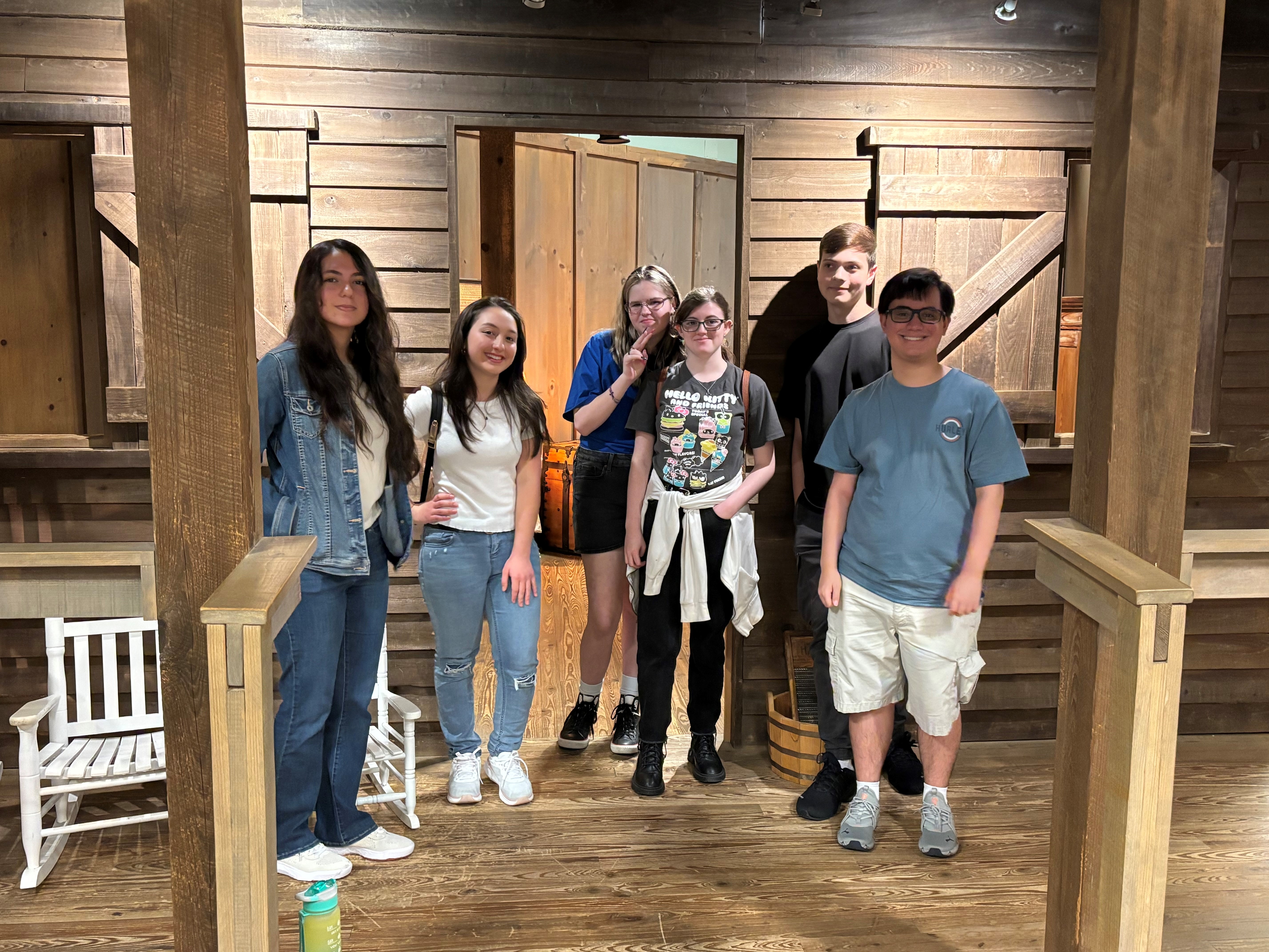 high school students stand in front of an old time cabin at a history museum