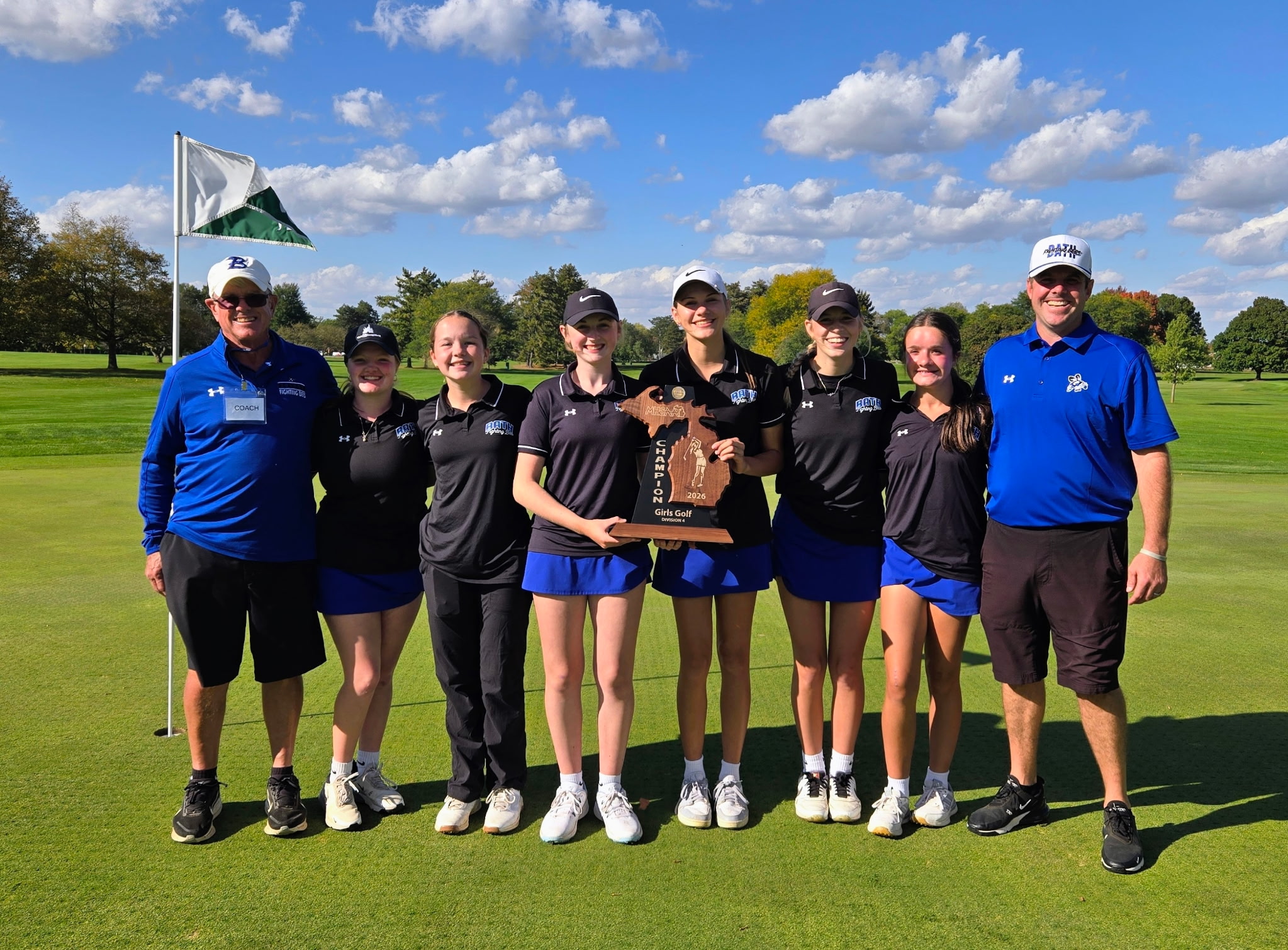 Girls golf team holding regional trophy standing with coaches