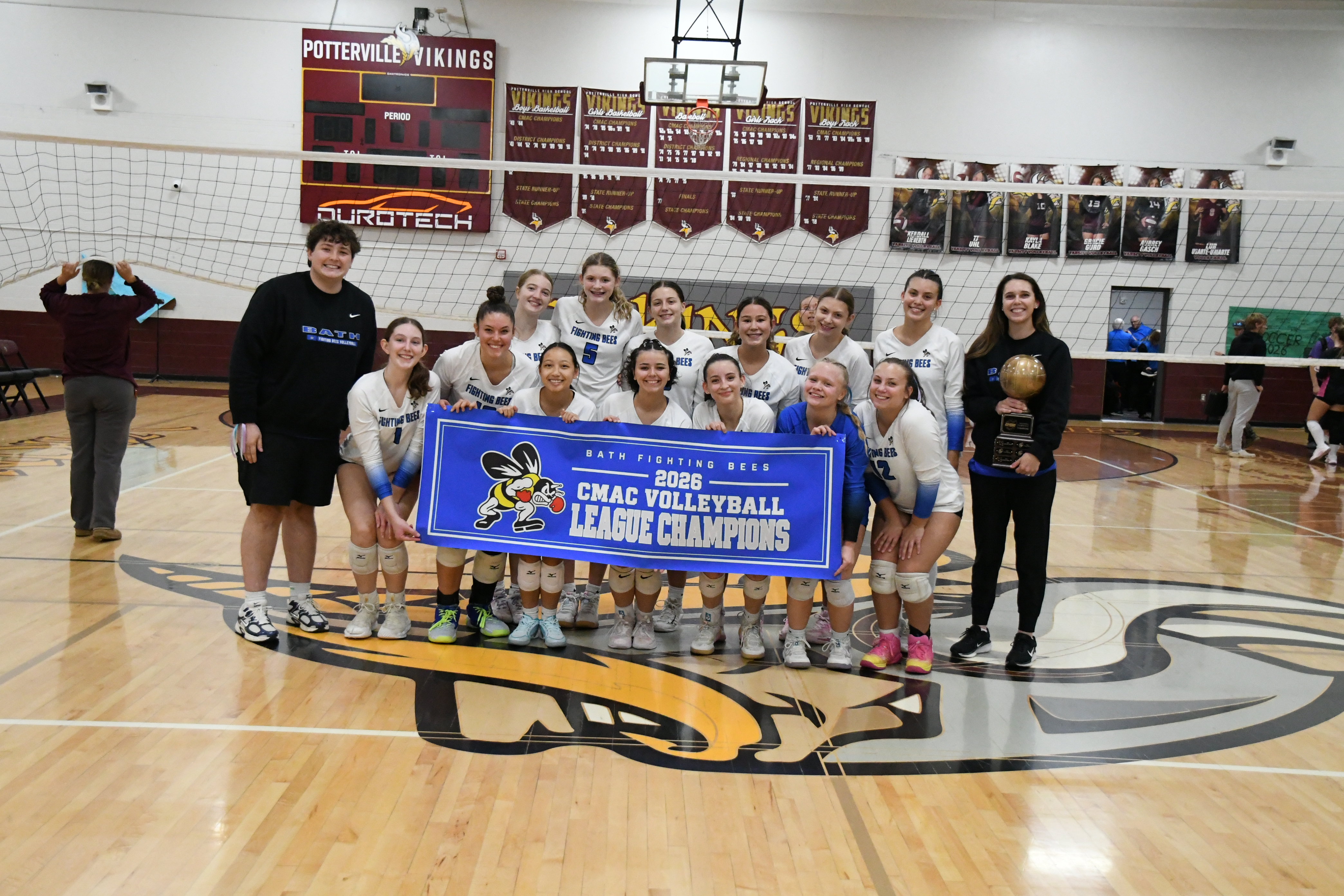 Girls varsity volleyball team holding CMAC league championship banner while the coach hold the league trophy