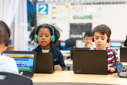 A girl and a boy are typing on their laptops at school desk.