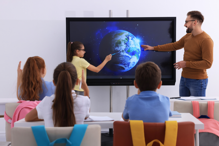 Teacher and a student are using an interactive board in front of  the class