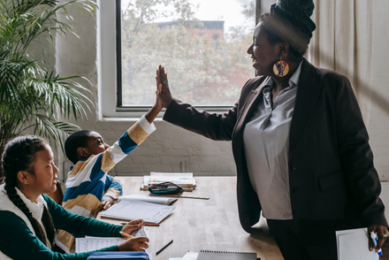 A female teacher is high-fiving two students in the classroom.