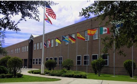 American flag in  front of numerous flags from varying countries in front of a red, brick school building