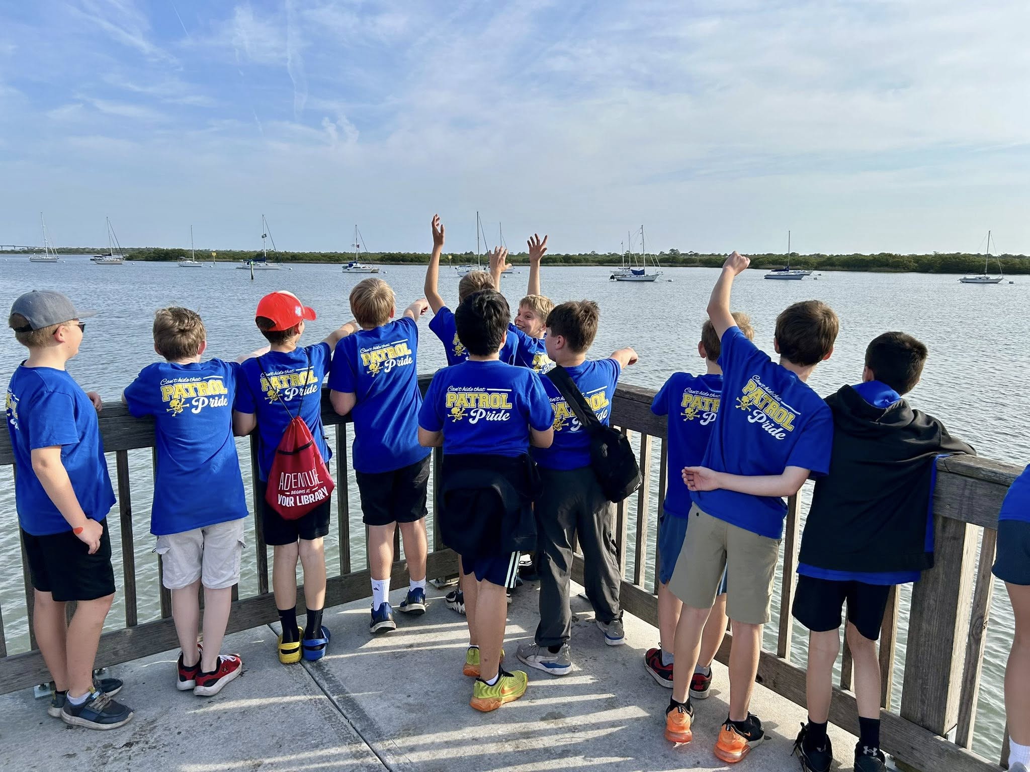 small group of young boys waving towards the water off of a pier