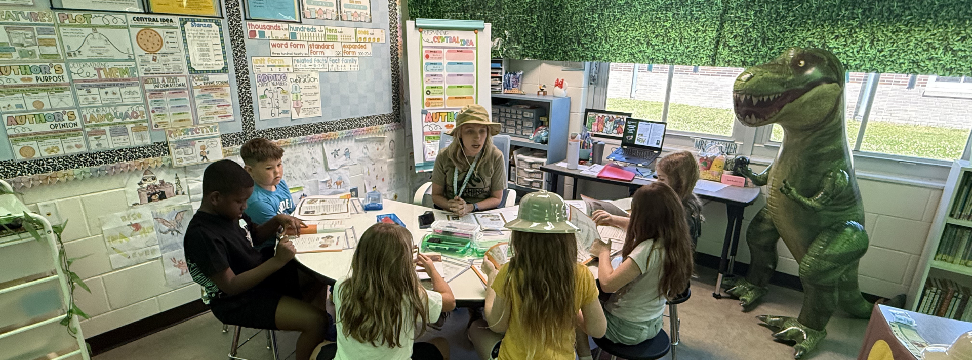 Group of second grade students sitting at table with teacher learning about dinosaurs