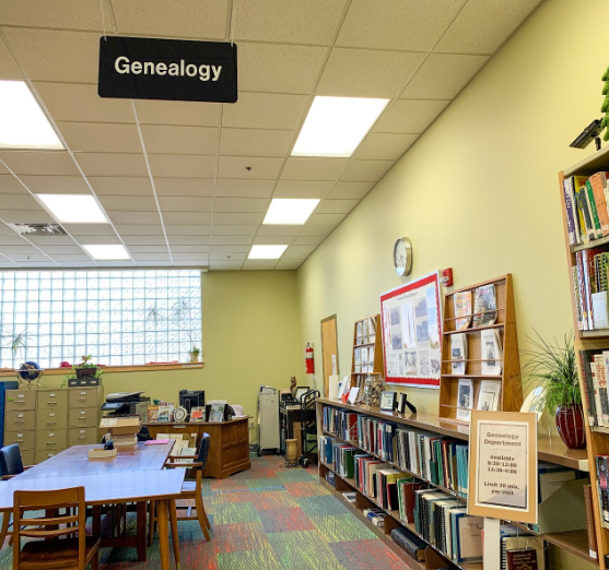 The Genealogy section of the Green County Public Library, equipped with a large research table and shelves stocked with extensive historical records, family documents, and microfilm readers for public use.