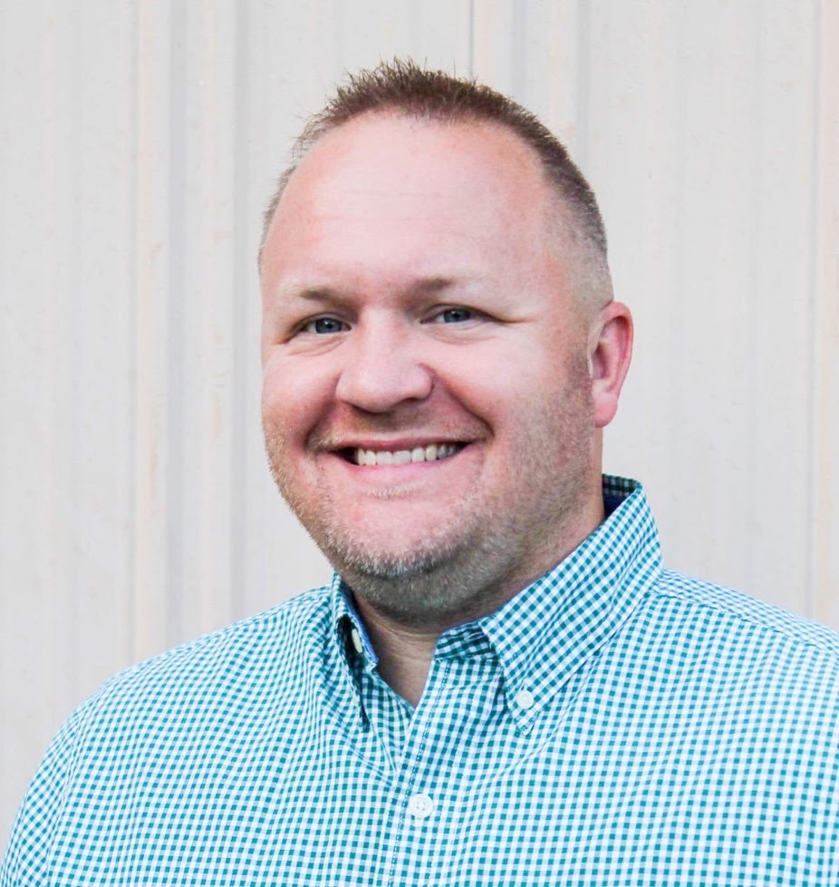 Headshot of Mayor John Shuffett smiling, wearing a blue and white checkered shirt.