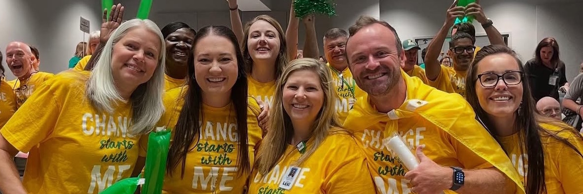 Administrators and employees wearing gold shirts stand smiling