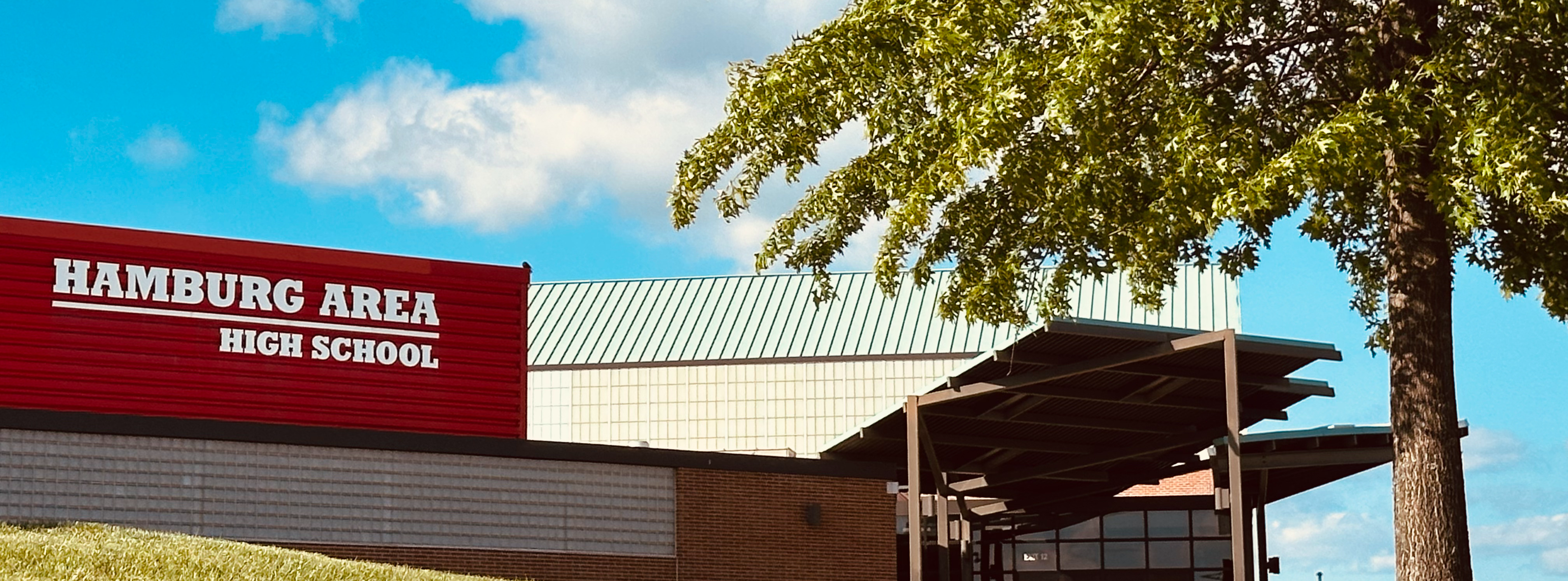 High School new gym entrance with Hamburg Area High School sign visible and tree in foreground. 
