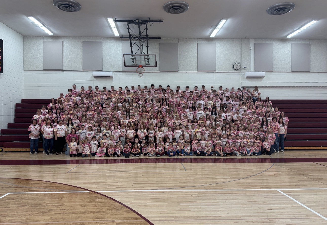 entire student body and staff in a group photo wearing maroon and gold tie dye shirts