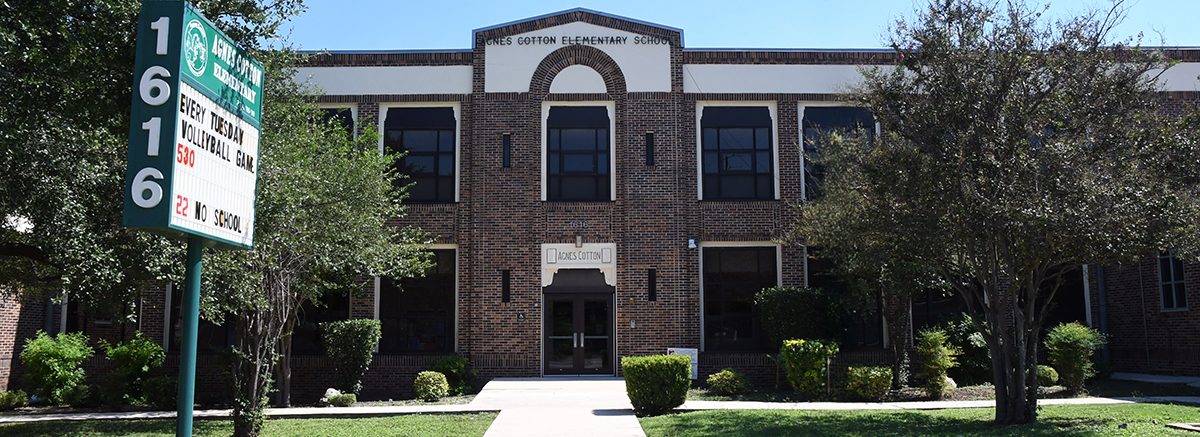 Entrance to Agnes Cotton Academy with lots of trees and bushes in the yard around the front of the building.