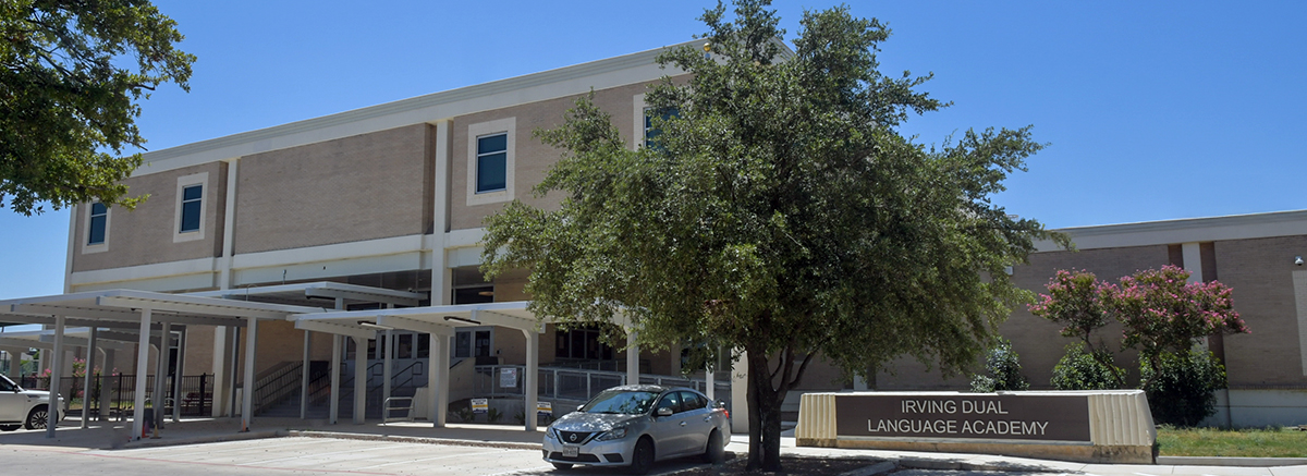 Front view of Washington Irving Sual Language Academy with 2 cars parked in front of school and big green tree in yard.