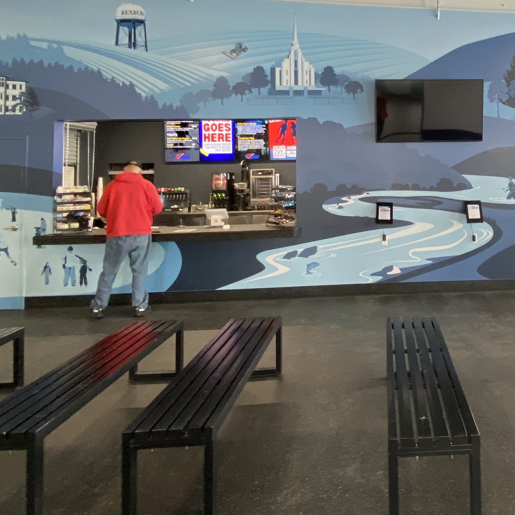 person at the check-in counter at the neutral zone that has a mural around it and benches