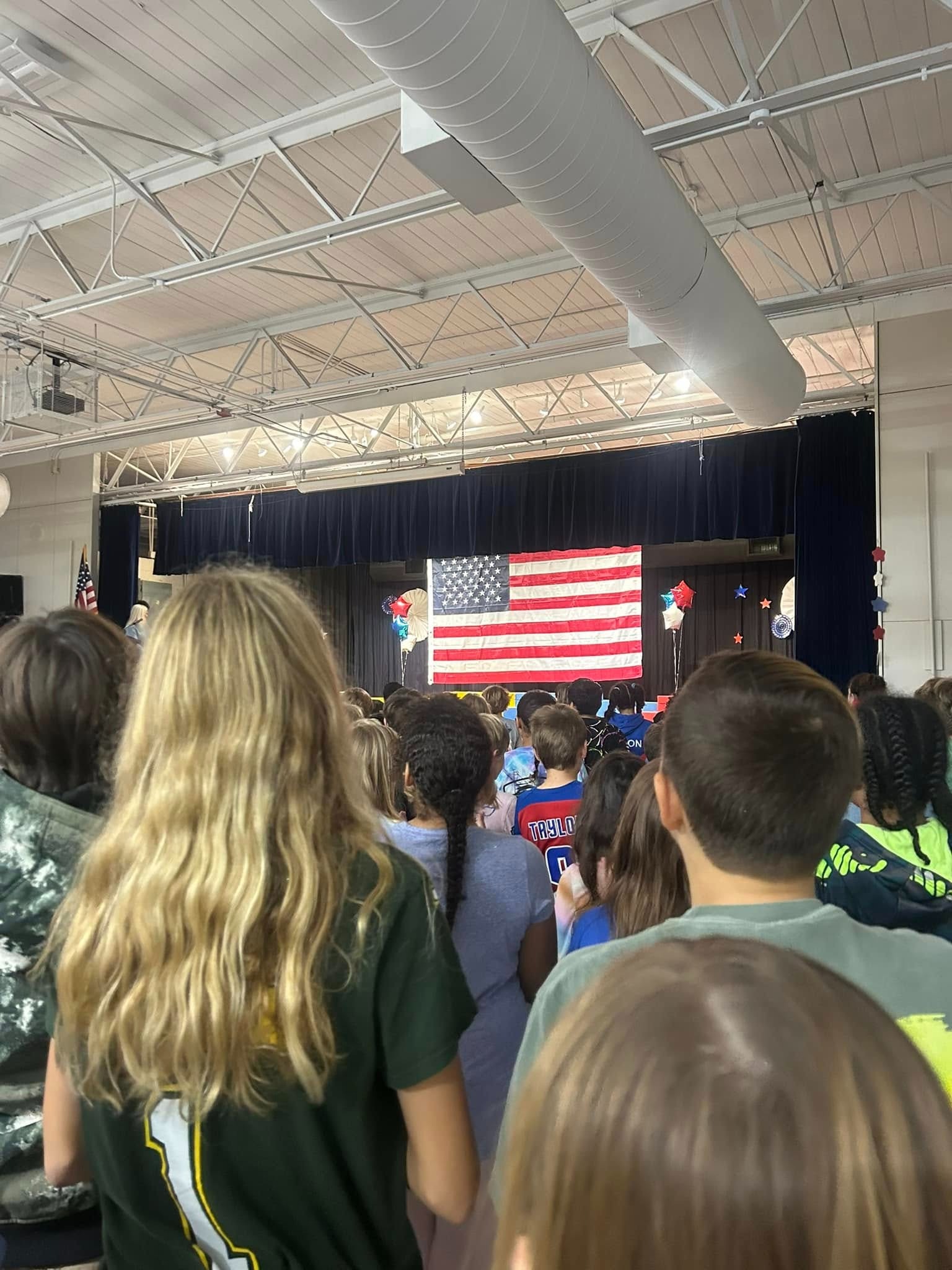 Image of a performing arts stage with a USA flag displayed.  Students are standing looking at the flag.