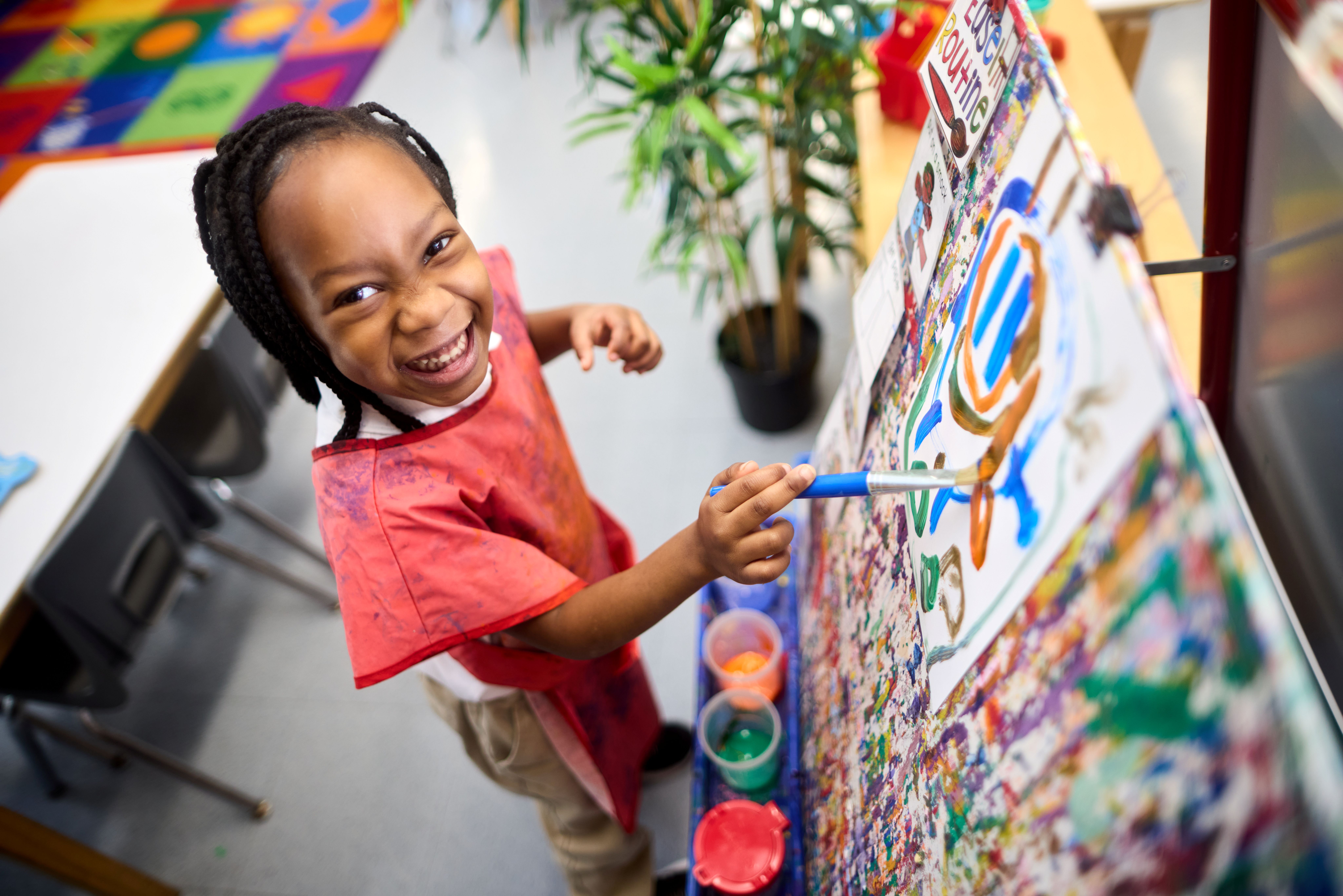 Student smiling while painting on an easel 