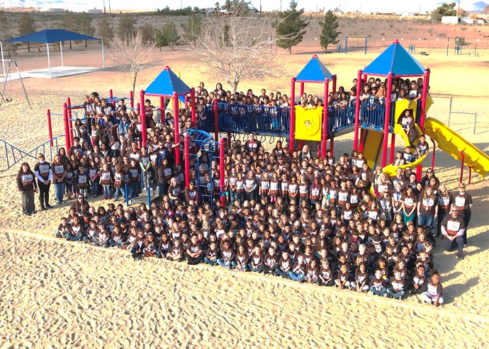 A group of children smiling and posing together in front of a colorful playground structure.