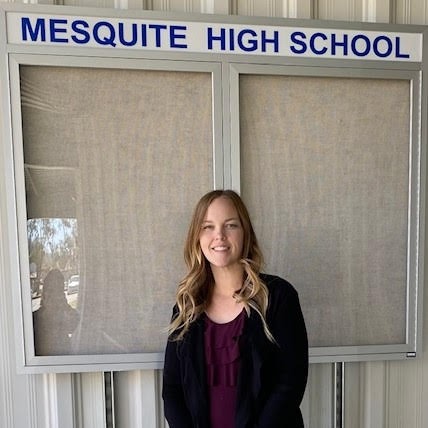 A woman stands in front of a sign for Mesquite High School, showcasing the school's name and logo.