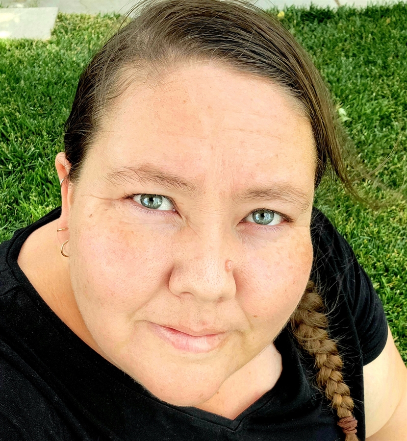1. A woman with blue eyes sitting on green grass, enjoying a peaceful moment outdoors. 2. A woman with blue eyes relaxes in the grass, surrounded by nature. 3. A woman with blue eyes sits in the grass, looking serene and contemplative.