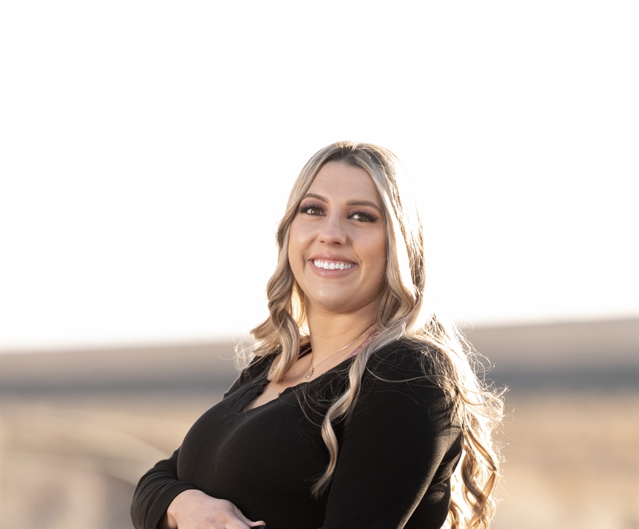 1. A woman wearing a black shirt stands in a grassy field, surrounded by nature. 2. A woman in a black shirt stands confidently in a lush green field under a clear sky. 3. A woman dressed in a black shirt poses in a vibrant field, showcasing the beauty of the outdoors.