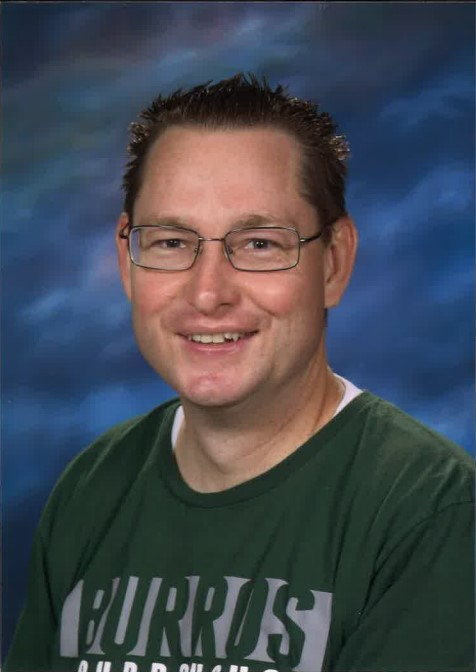 1. A smiling man wearing glasses and a green shirt, exuding a friendly and approachable demeanor. 2. A cheerful man in glasses and a green shirt, smiling warmly at the camera. 3. A man with glasses and a green shirt, smiling happily, conveying a sense of friendliness.
