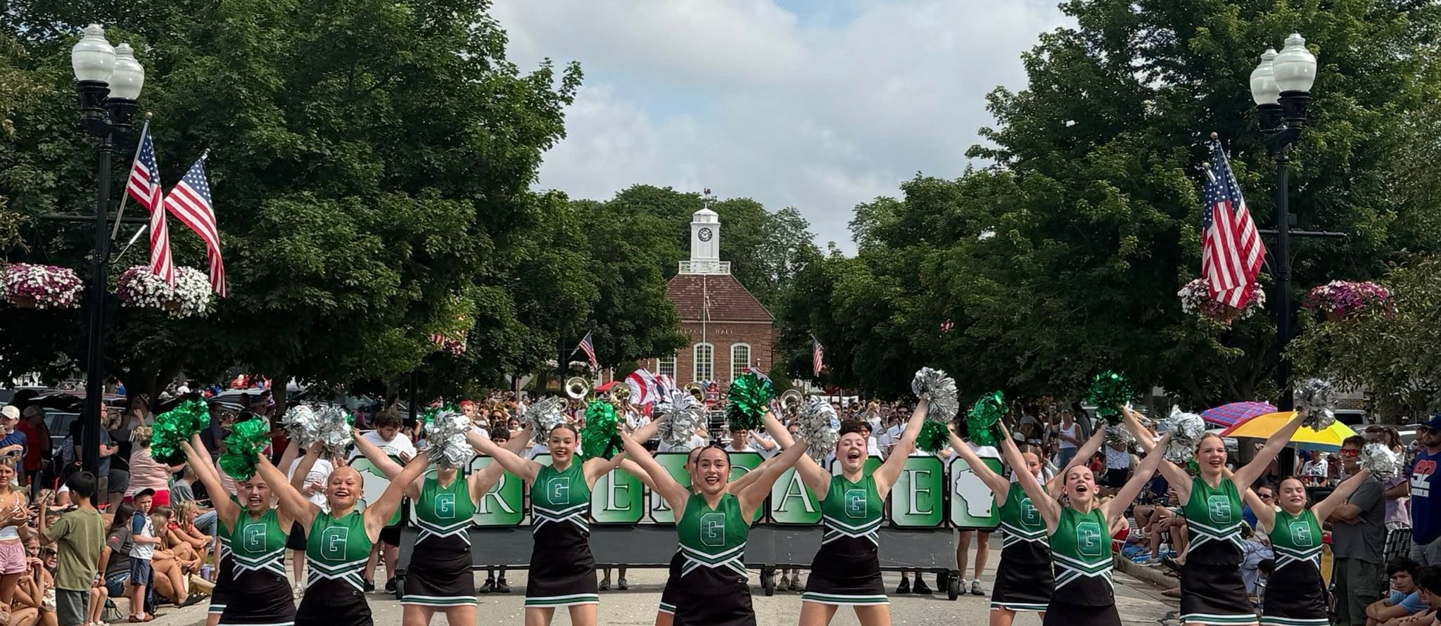 Students in poms squad outfits standing on a street with hands up in a cheer pose