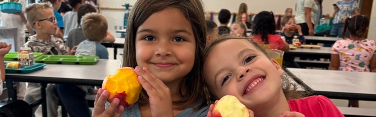 Students smiling at the lunch table holding fruit