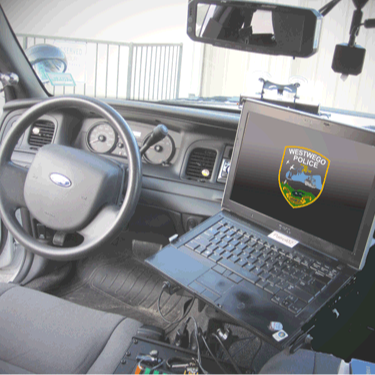 Inside of a police vehicle, the steering wheel, dashboard, and laptop