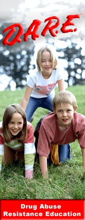 D.A.R.E. Drug Abuse Resistance Education Post with three children forming a triangle formation on their needs on grass.
