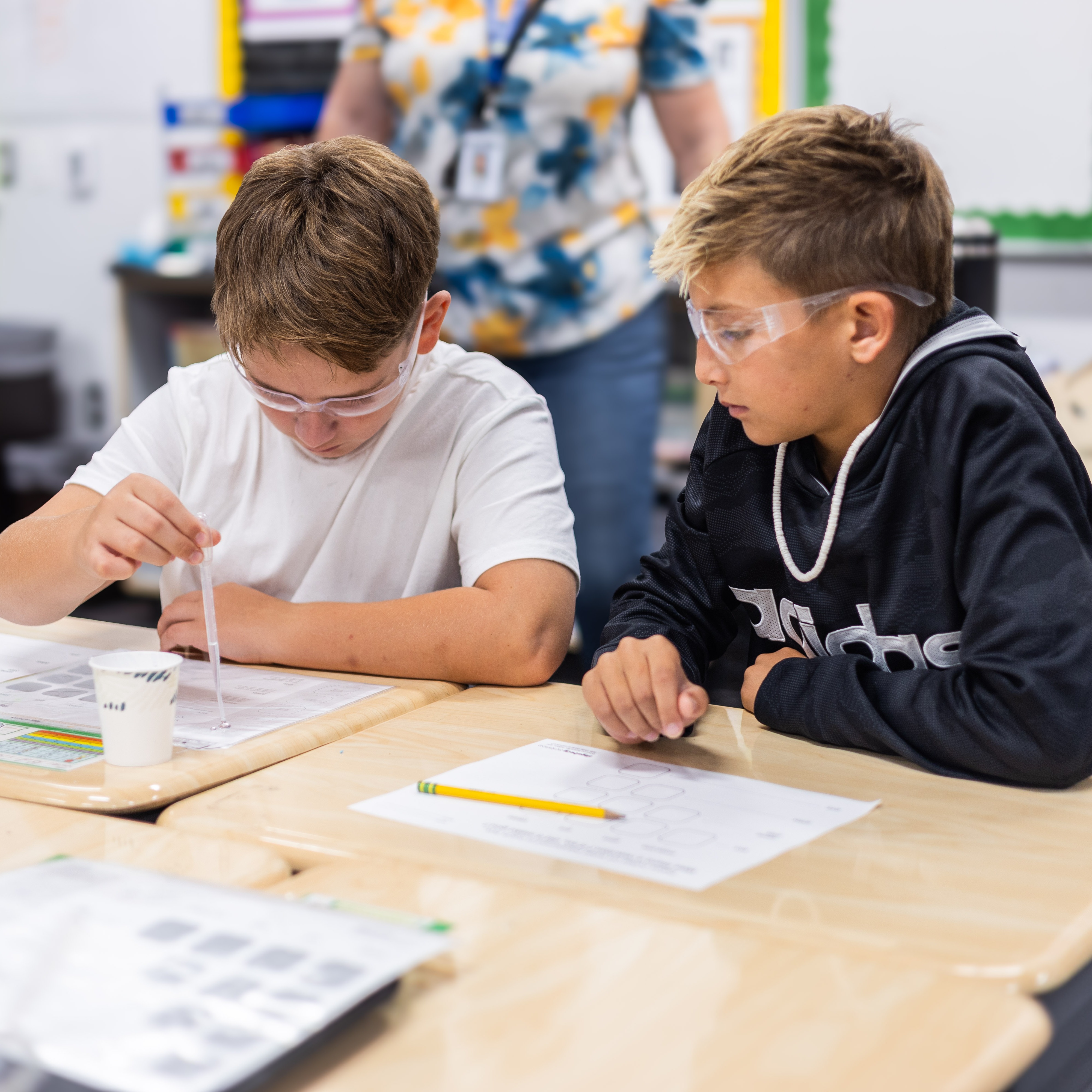 two students wear protective glasses and engage in a science experiment