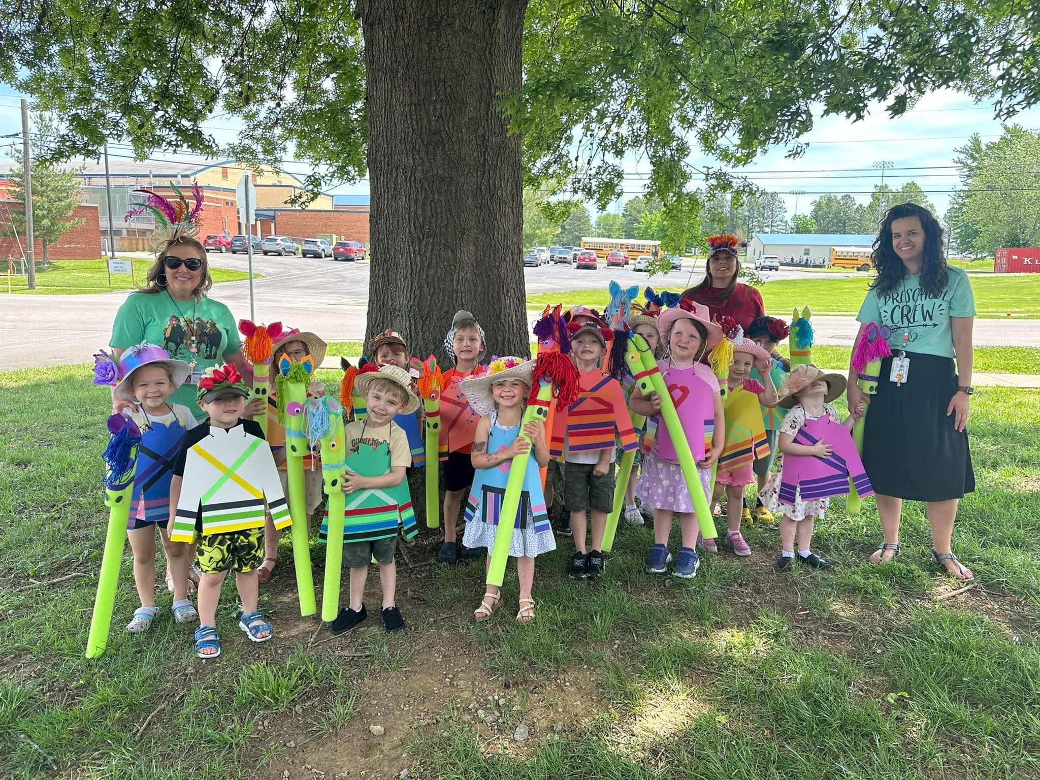 preschoolers and teachers outside in derby hats with pool noodle "race horses"