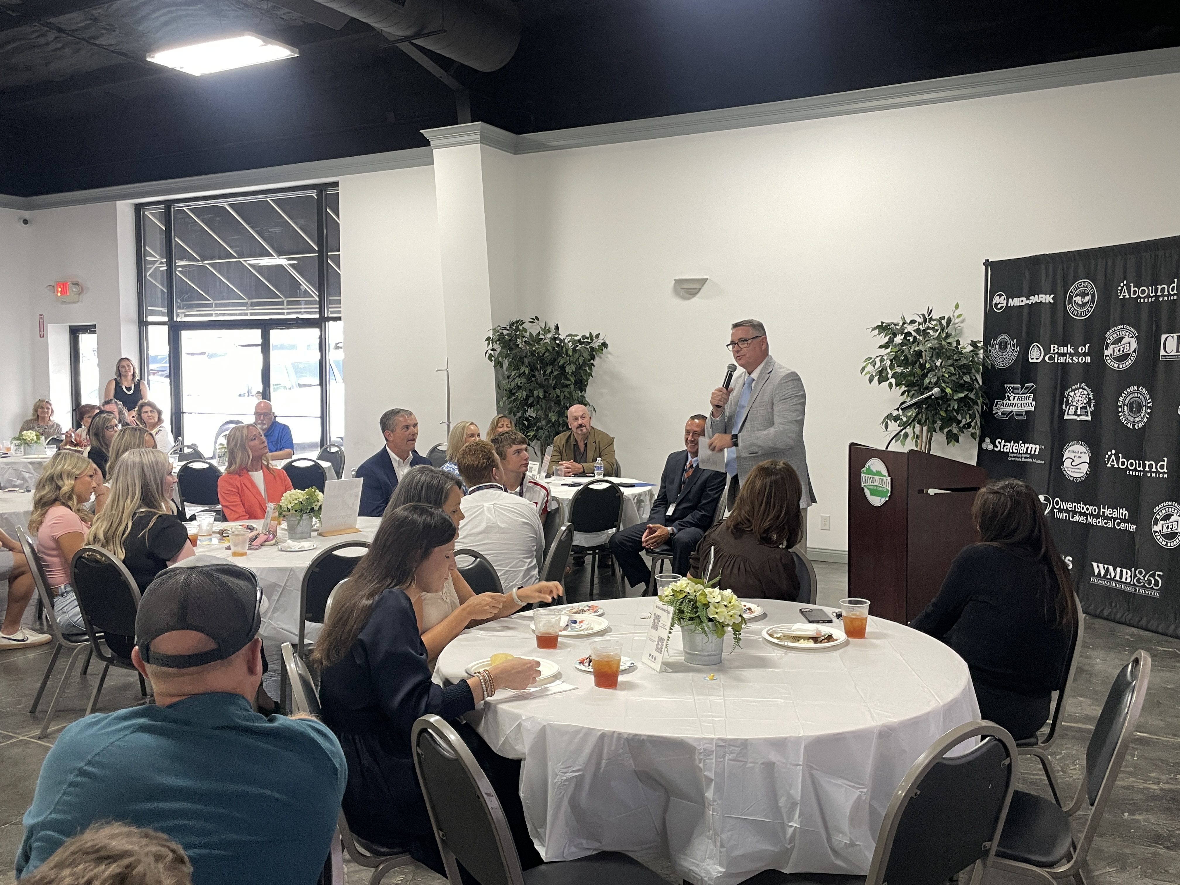 Man with mic and notes talking to luncheon crowd